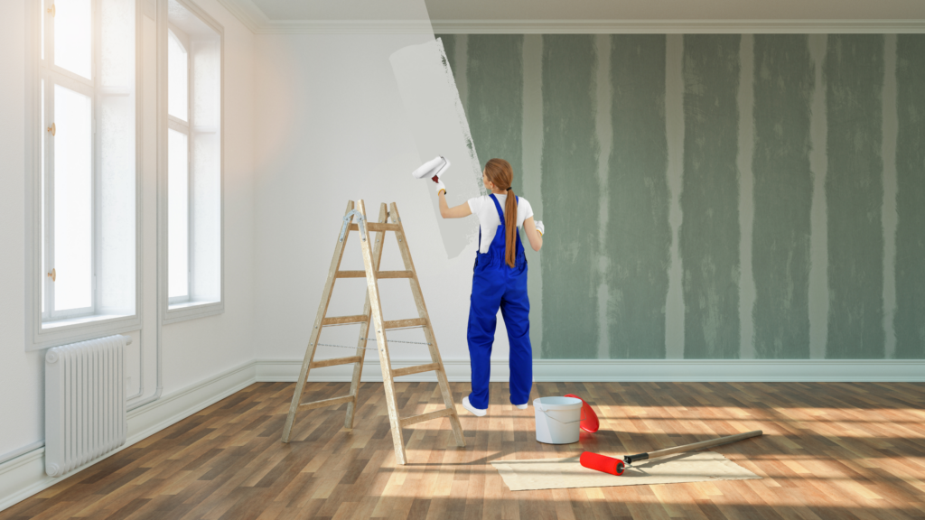 A person applying white paint to a living room wall, brightening the space and making it more shoot-ready.