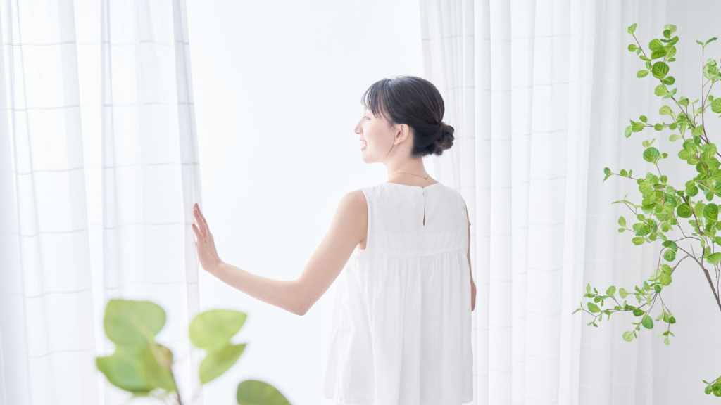 A homeowner arranging light, sheer curtains in a sunlit living room to enhance natural lighting.